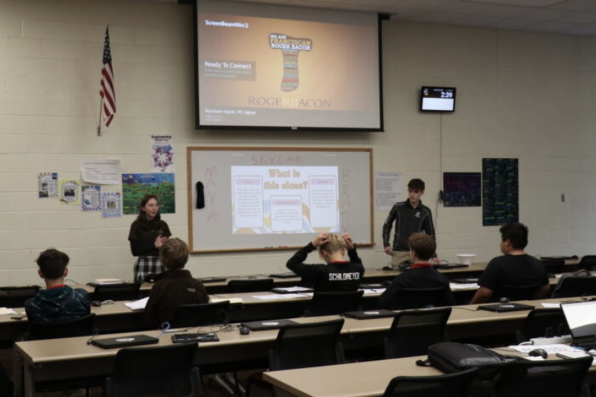 A classroom at Roger Bacon: two student instructors presenting at the front of the room while eighth graders work at their desks.